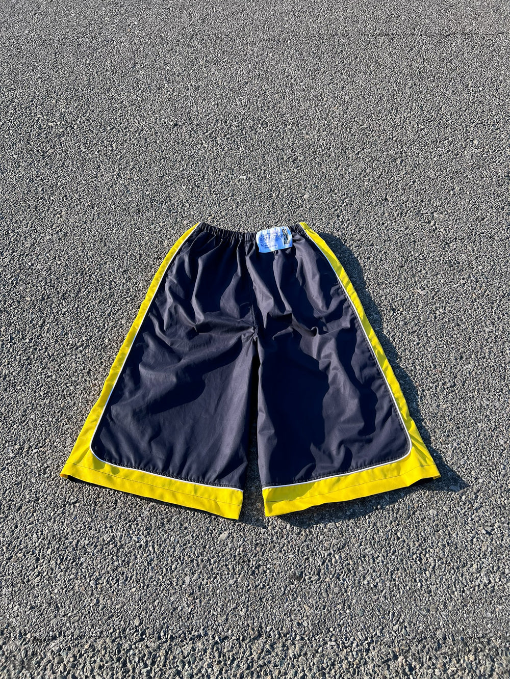 Pantaloncini sportivi EMANUELE MONACO STORE blu scuro con inserti gialli e profili bianchi, taglio ampio e tecnico.